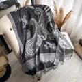 Elegante scialle di cashmere paisley grigio e nero con frange su una poltrona - Grigio