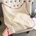 Beige pleated silk scarf with contrast red scalloped edge held against a sofa - Large Square / Apricot