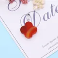 Red agate four-leaf clover pendant with natural textures and silver clasp on a blue desk - Red Agate