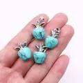 Set of four apple-shaped turquoise stone pendants with silver leaf details held in hand - Blue Turquoise