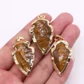 Gros plan de pendentifs flèches en oeil de tigre avec bords dorés tenus à la main - Œil de tigre