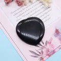 Polierter herzförmiger schwarzer Obsidian auf dekorativer Blumenkarte im Hintergrund - Schwarzer Achat