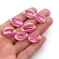 Close-up of hand holding colorful painted natural cowrie shells for DIY jewelry making - Style 9 (Pink with Green Dots)