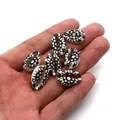 Detailed view of hand holding small black and white floral printed natural cowrie shells - 9x19mm (20 Pieces/Pack) / No. 6 (Black and White Floral Geometric)