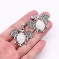 Close-up of bat-shaped alloy pendants with natural stone inlay held in a hand - White Jade
