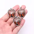 Detailed view of tree of life heart pendants with goldstone held by hand for scale - Gold Sandstone