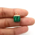 Detailed close-up of malachite cube pendant with gold metal loop held by fingers - Malachite
