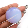 Hand holding a round opalite stone pendant with gold plating for jewelry making - Opal