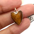 Close-up of heart-shaped tiger eye stone pendant with gold plated rim shown for scale - Tiger's Eye