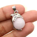Close-up of a silver dolphin pendant holding a round pink natural stone on a person's hand - Dolphin Shape / White Jade