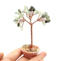 Mini handmade green crystal bonsai tree with copper wire and pink base held by fingers - Prehnite