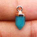 Detailopname van een zeshoekige turkooizen kristallen hanger vastgehouden tussen vingers - Blauwe Chalcedoon