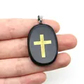 Gros plan d'un pendentif ovale en pierre noire avec une croix dorée tenu en main - Agate noire