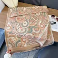 Dettaglio di scialle con motivo paisley e frange su tavolo in legno con accessori - Stile con nappine e stampa paisley / Cachi