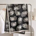 Leaf print cashmere scarf in black and beige, draped on a hanger with elegant styling - 185x65cm / Black