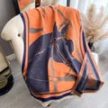 Detail of a thick orange equestrian shawl with horse head jacquard and fringe on leather sofa - Orange Blue