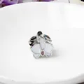 Macro detail of orchid charm with white enamel petals and pink gemstone for DIY bracelets - White