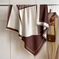 Dettaglio di uno scialle geometrico marrone e beige con frange su un appendiabiti - Caffè