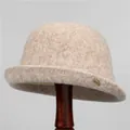 Dettaglio cappello a campana in lana beige con fibbia a foglia dorata su legno - M / Beige