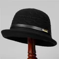 Detail of black knit cloche hat with leather strap and gold buckle on a wooden stand - M (56-58cm) / Black