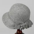 Detail view of a grey wool cloche hat with a bow and fur ball on a wooden stand - M (56-58cm) / Gray