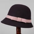 Detail of wool cloche hat featuring pink knitted ribbon and bow on wooden stand - M (56-58cm) / Purple