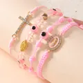 Vista macro dei braccialetti rosa intrecciati con medaglia della Madonna e ciondolo a croce - Rosa