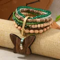 Detalle de pulsera bohemia con cristales verdes y un colgante de mariposa de madera tallada - Multicolor