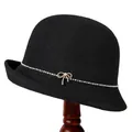 Elegante zwarte gebreide cloche hoed met strass strik en parel op een houten hoedenstandaard - M / Zwart