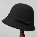 Detail of a vintage black wool cloche hat with a flat bow on a classic wooden stand - M (56-58cm) / Black