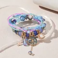 Detalle de pulseras de varias capas con cuentas azules y violetas y dijes dorados - Azul