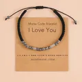 Handmade black woven Morse code bracelet featuring 'I Love You' message on a kraft card - Morse Code I Love You