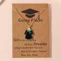 Golden graduation gown necklace with green enamel pendant on a kraft paper display card - Academic Gown Style 4