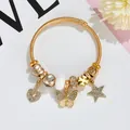 Detail of a gold coil bracelet featuring rhinestone heart, star, and butterfly charms - White