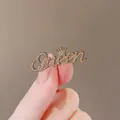 Golden Queen letter brooch with crown and white rhinestones held by hand - Queen