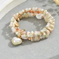 Detalle de una pulsera multicapa con cuentas color crema y un colgante de corazón - Estilo Colgante Perla Corazón / Marrón