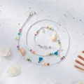 Détail de la chaîne de lunettes perlée avec coquillages et glands sur fond de sable - Blanc