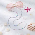 Detail van kleurrijke kralen brillenketting met gouden hartbedeltje op roze zonnebril - Veelkleurige Polymeerklei