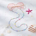 Nahaufnahme bunte Brillenbead-Kette mit Herzanhängern auf feinem Sandstrand-Hintergrund - Buntes Herz