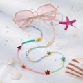 Detail van kleurrijke kralen brillenketting met LUCKY bedeltjes op een wit zanddecor - Gekleurde Zeester
