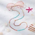 Detail der Brillenlkette mit LOVE-Buchstaben und bunten Perlen auf weißem Strand im Sand - Kontrast Love Ton