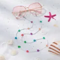 Detail van roze zonnebril met kleurrijke kralenbloemenketting op zacht wit zand - Kleine Witte Bloem