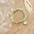 Detalle de pulsera de cristal verde con colgante de margarita y toques metálicos dorados - Verde