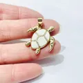 Zirconia sea turtle pendant in gold finish held by hand to show compact product size - Gold Turtle (Cream Enamel)