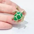 Golden sea turtle pendant with green enamel and white zircon inlay shown in hand - Gold Turtle (Emerald Enamel)