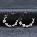 Detailed close-up of gold hoop earrings with white floral accents on black leather - Silver
