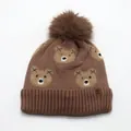 Dettaglio della trama in maglia di un cappello invernale marrone con orsetti e pompon - Taglia unica / caffè