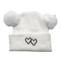 Close-up of white knit baby hat featuring dual fluffy pom-poms and black heart embroidery - One Size / White