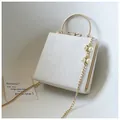 Detail of white evening bag with golden ring handle, pearl charm and bow clasp - Simple Version / White