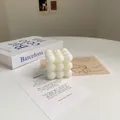 Gros plan sur une bougie cube en cire de soja minimaliste posée sur un livre blanc - Bubble Cube Blanc (Freesia)